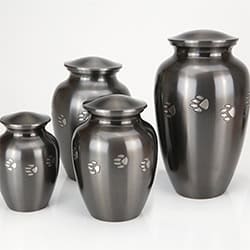 Four metallic urns of varying sizes are displayed together, each with a shiny finish and decorated with small paw prints. Ideal for pet cremation in Harris County, TX, these urns feature domed lids and are set against a plain background.
