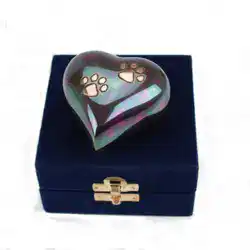 A heart-shaped, iridescent urn with gold paw prints—ideal for pet cremation in Harris County, TX—rests on a closed, dark blue velvet box with a gold clasp.