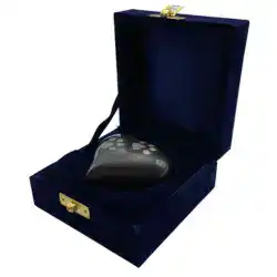 A black heart-shaped object with white markings sits inside an open dark blue velvet box, lined with matching fabric and secured with a gold clasp—an elegant tribute often chosen for pet cremation in Harris County, TX.