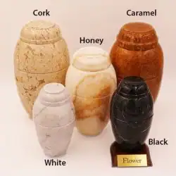 Five stone urns in different colors—Cork, Caramel, Honey, White, and Black—are arranged together for pet cremation in Harris County, TX. The Black urn sits on a small wooden base labeled “Flower.”.