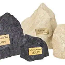 Several pet memorial stones in different shapes and colors, each with a brass plaque engraved with messages like "In Loving Memory MOLLY" and "LUCY"—a thoughtful tribute for those seeking pet cremation in Harris County, TX.