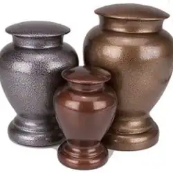 Three metallic urns of different sizes and colors—one dark gray, one bronze, and one dark brown—are placed side by side with rounded bodies, wide bases, and lids, suitable for pet cremation in Harris County, TX.