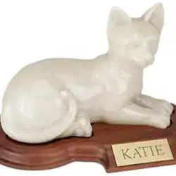 A white ceramic cat figurine lies on a brown wooden base with a gold nameplate that reads "KATIE," often used as a memorial for pet cremation in Harris County, TX.