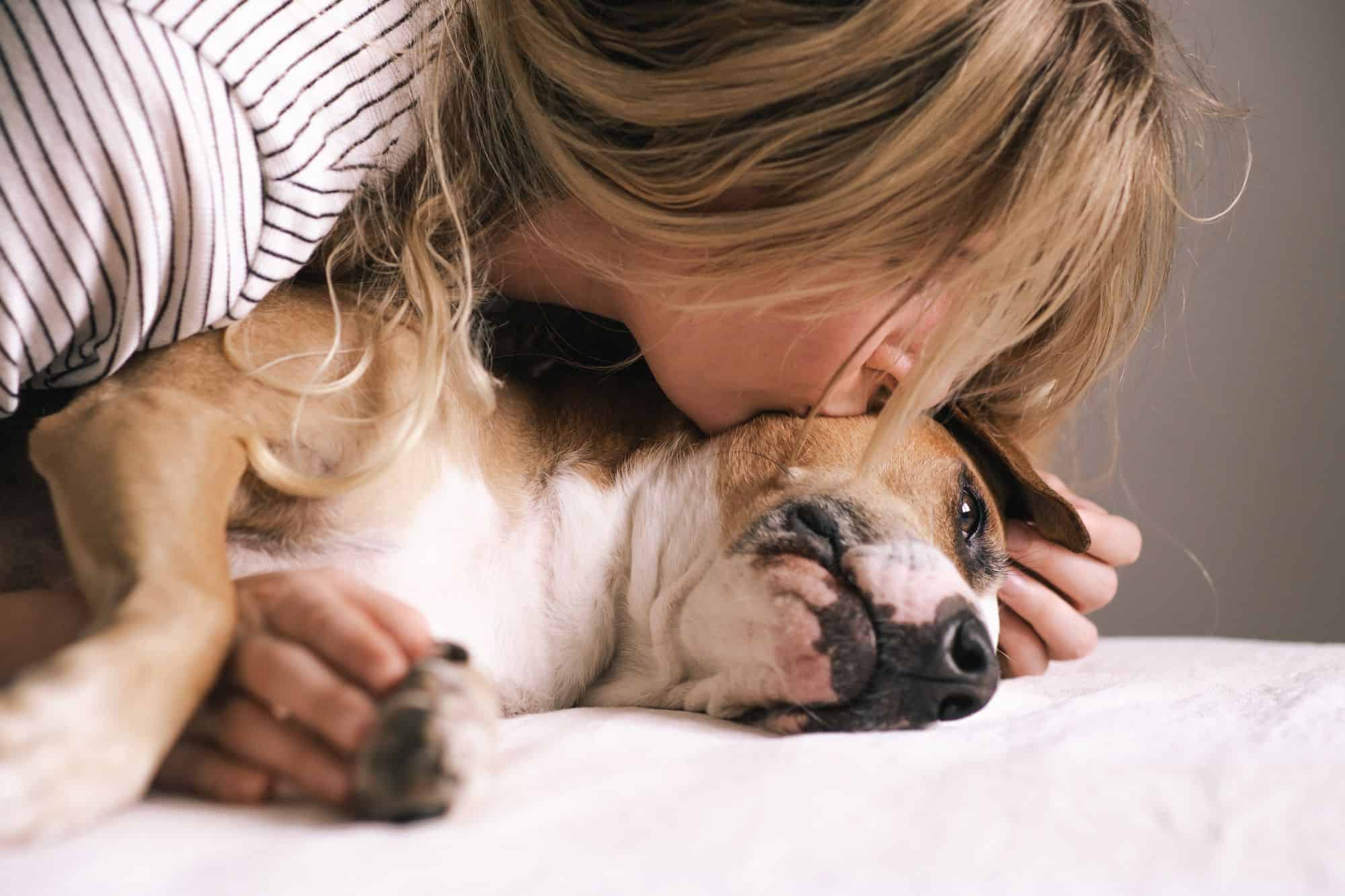 A woman hugs and kisses her dog on a bed, sharing gentle affection—At-Home Pet Euthanasia Harris County.