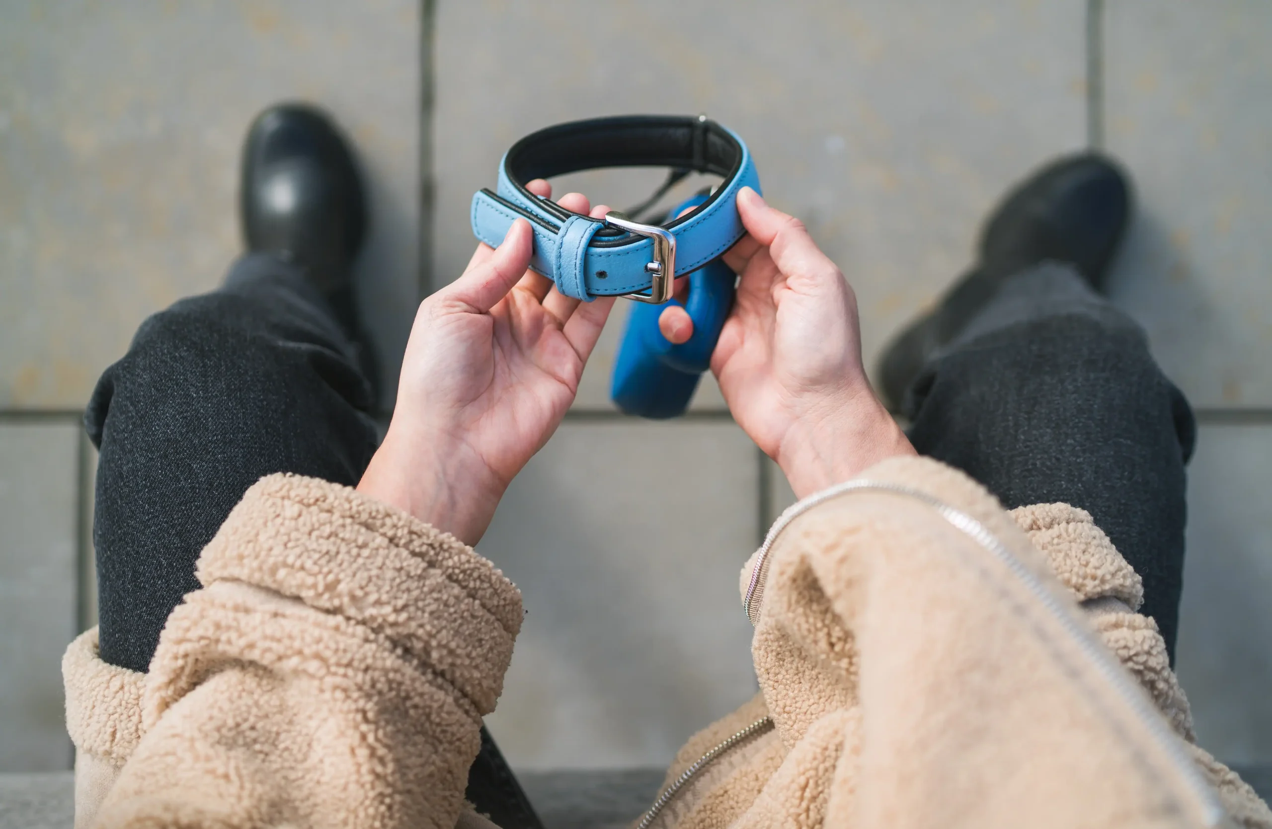 Person in a tan coat holds a blue dog collar while standing on gray tiles in Harris County, TX.