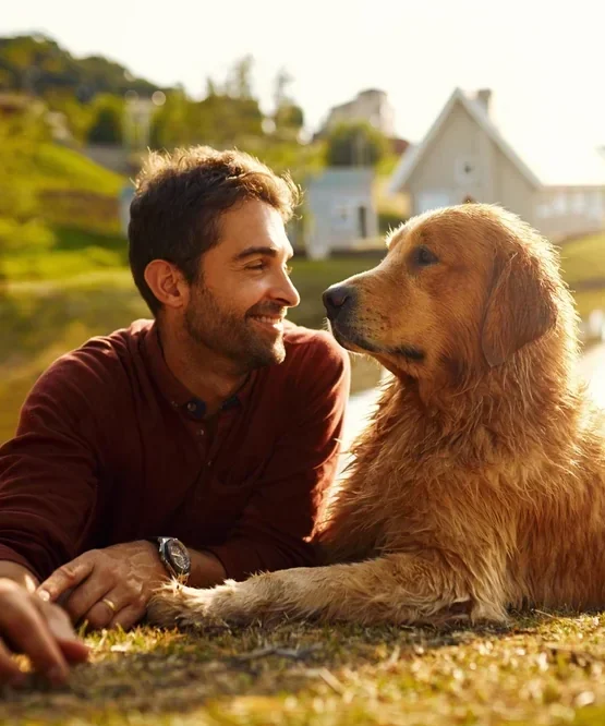 A man relaxes on the grass, smiling at his golden retriever on a sunny day in Harris County.