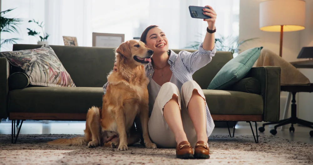 A smiling woman sits on the floor with her golden retriever in their cozy TX home, sharing happy moments.